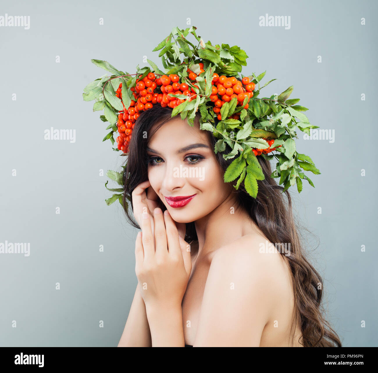 Brünette Frau lächelnd. Happy fashion model Mädchen mit gesunden curly Frisur, Make-up und roten Beeren und grüne Blätter Stockfoto