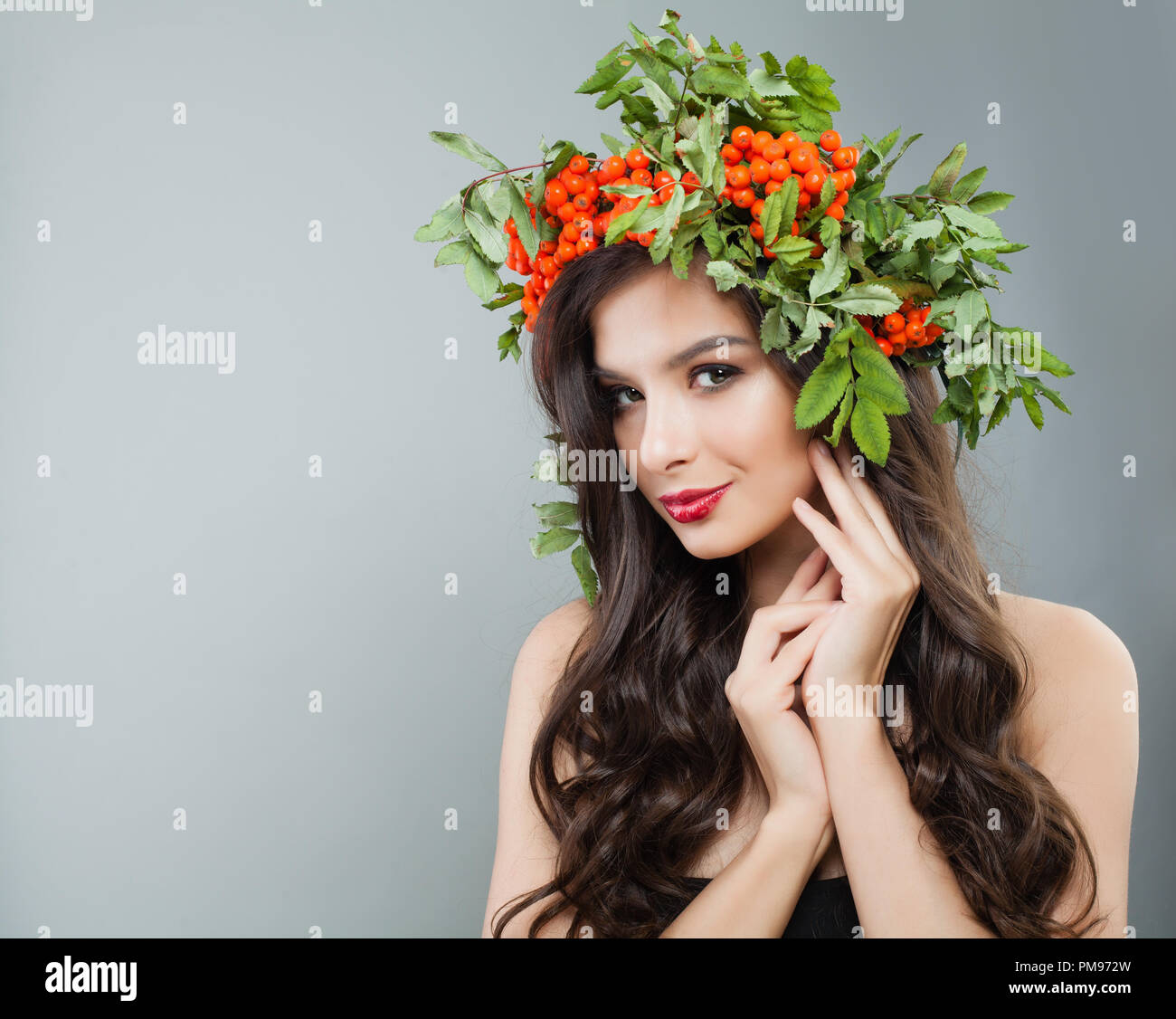 Attraktive Frau Mode Modell mit gesunden lockige Haare, Make-up und roten Beeren und grüne Blätter Kranz Stockfoto