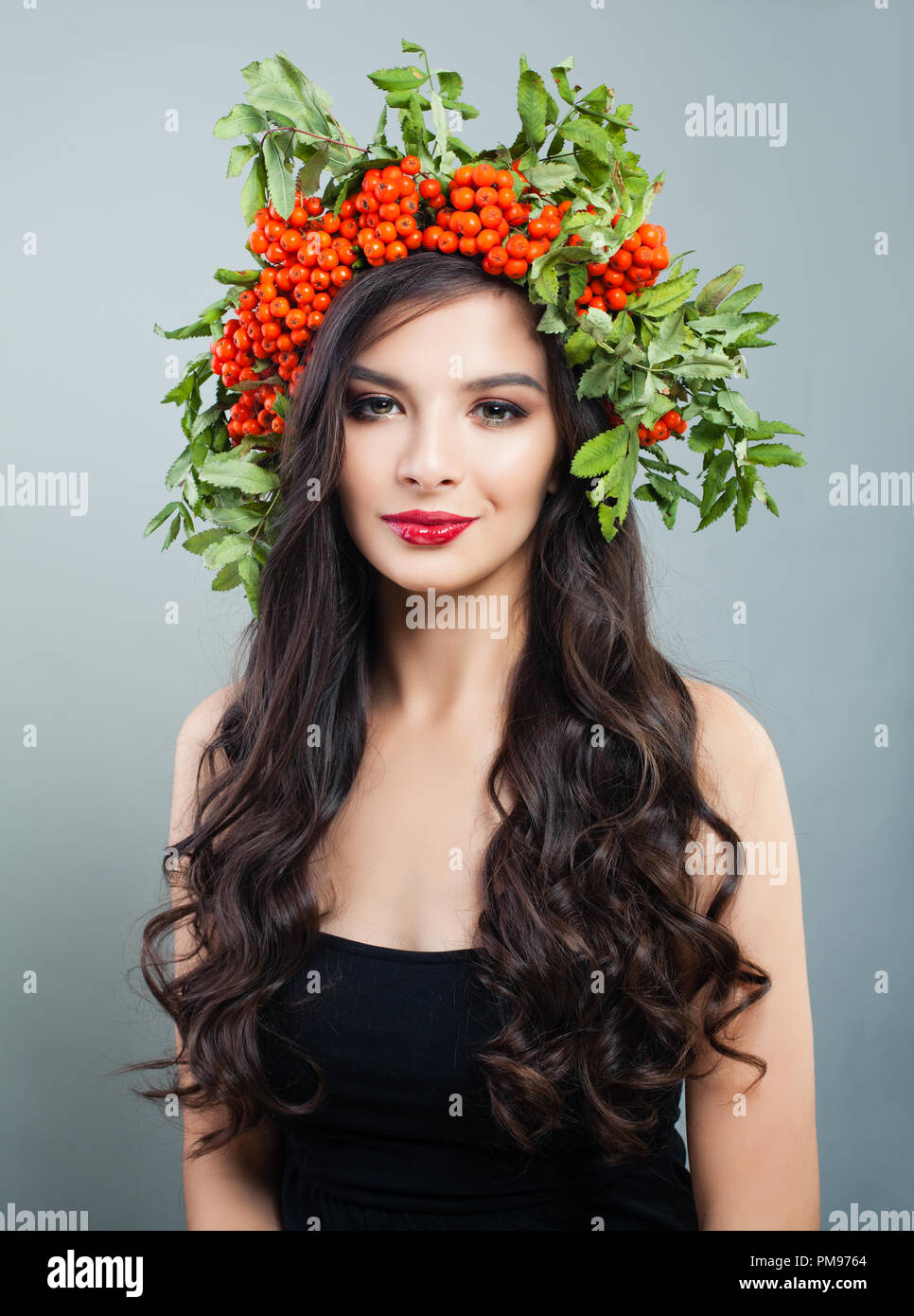 Hübsche brünette Frau Mode Modell mit gesunden curly Frisur, Make-up und roten Beeren und grüne Blätter, Porträt Stockfoto