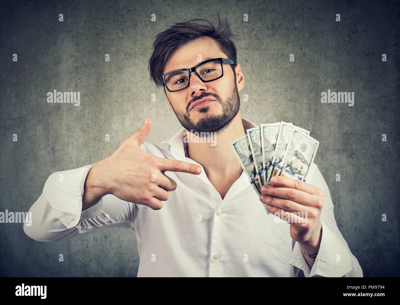 Junge Mensch auf der Suche super arrogant und zeigt Haufen Bargeld Dollar auf grauem Hintergrund Stockfoto
