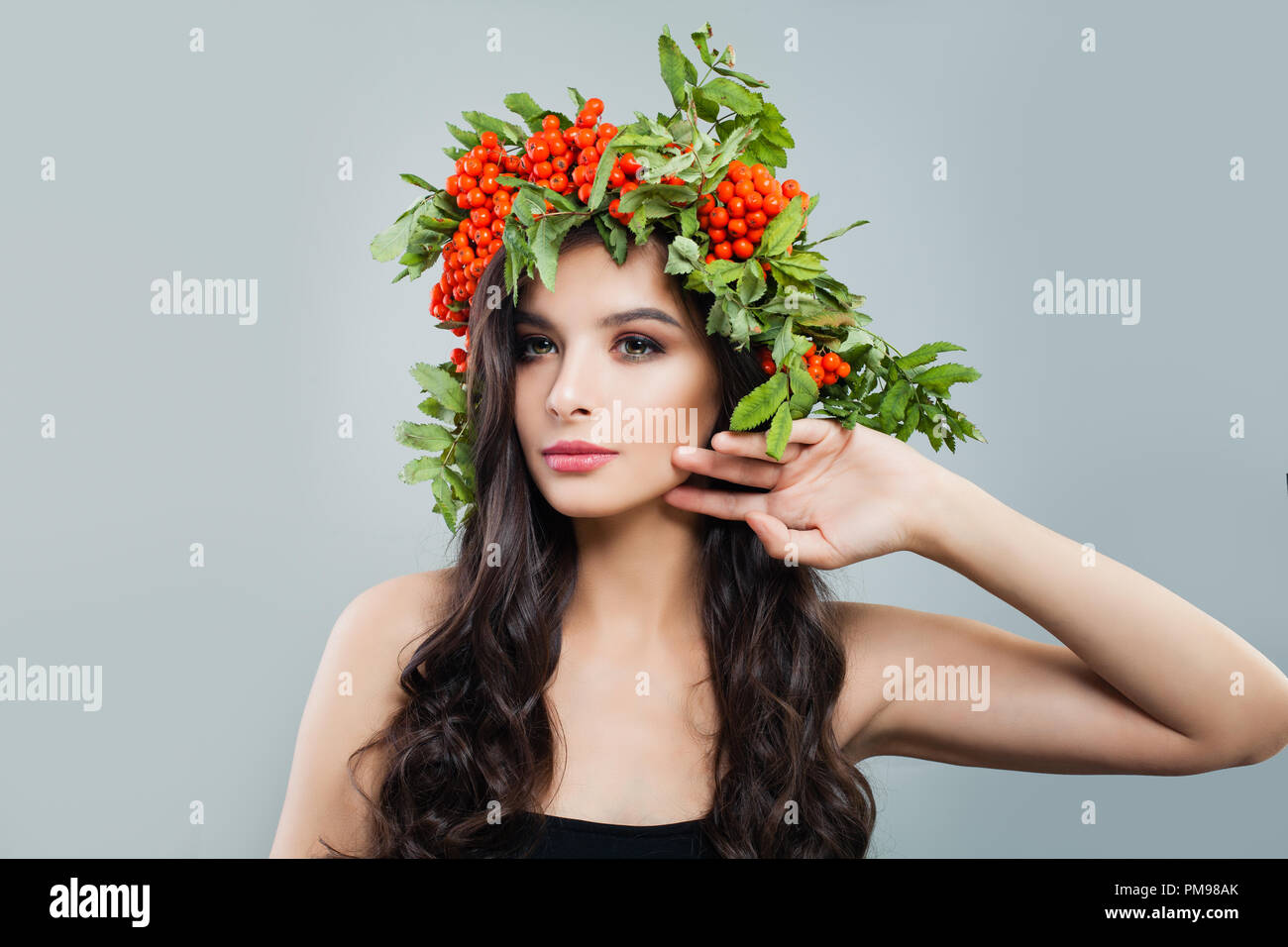 Schöne Frau mit gesunden lockiges Haar und natürliches Make up tragen in roten Beeren und grüne Blätter Kranz Stockfoto