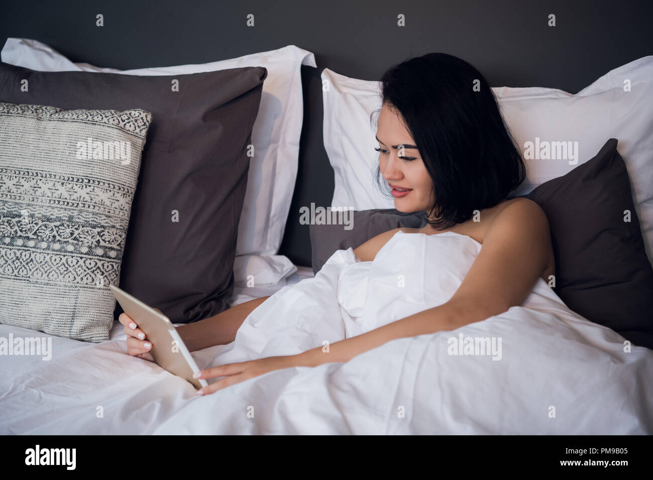 Eine lächelnde Frau liegt auf dem Bett Blättern durch Ihr Tablet. Stockfoto