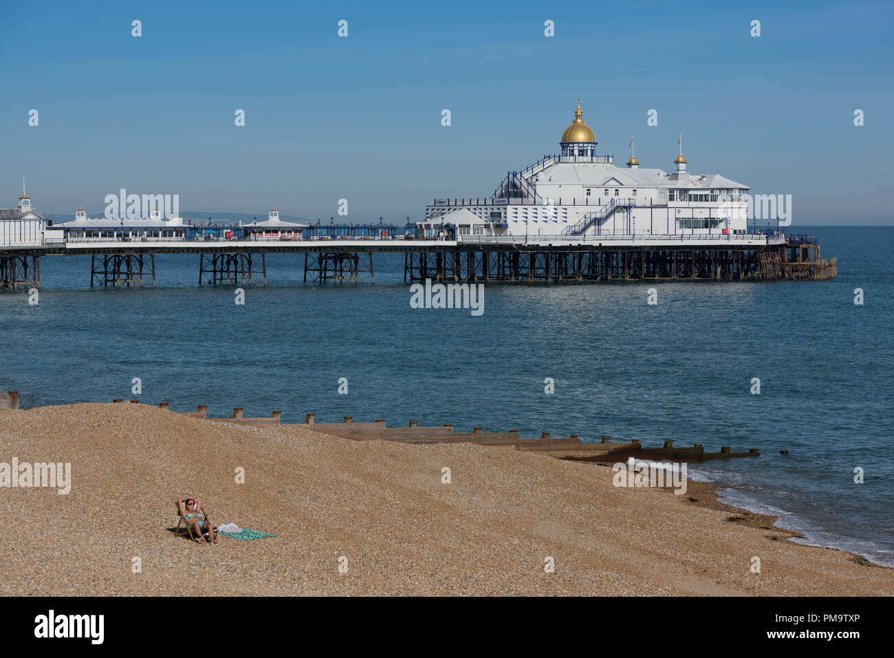 Ein einsamer Sonnenanbeter am Strand von Brighton in der Grafschaft East Sussex an der Südküste von England mit der Pier hinter sich. Stockfoto