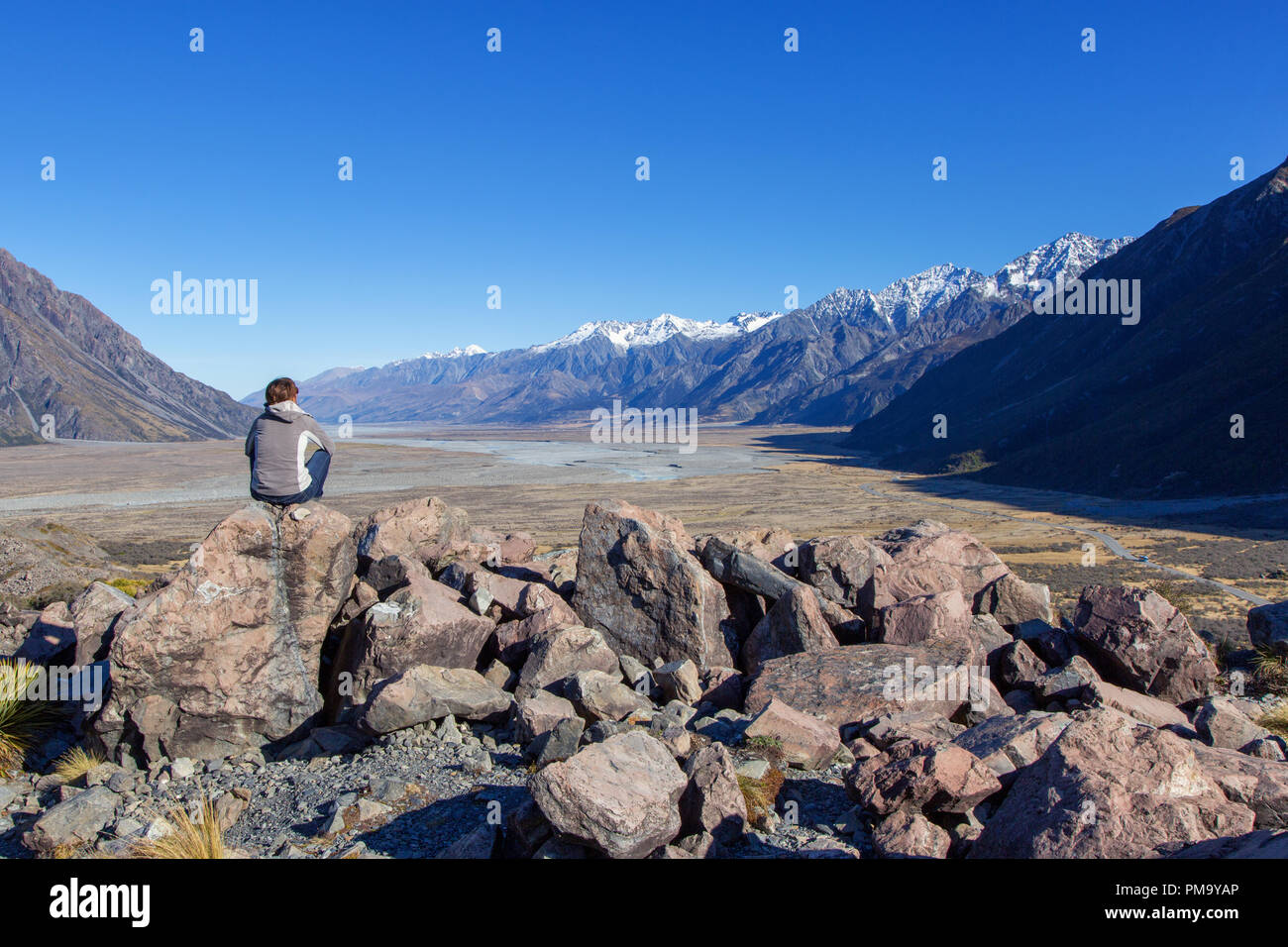 Person sitzt in Aoraki Mount Cook Nationalpark vor einem weiten Tal, Neuseeland, Südinsel Stockfoto
