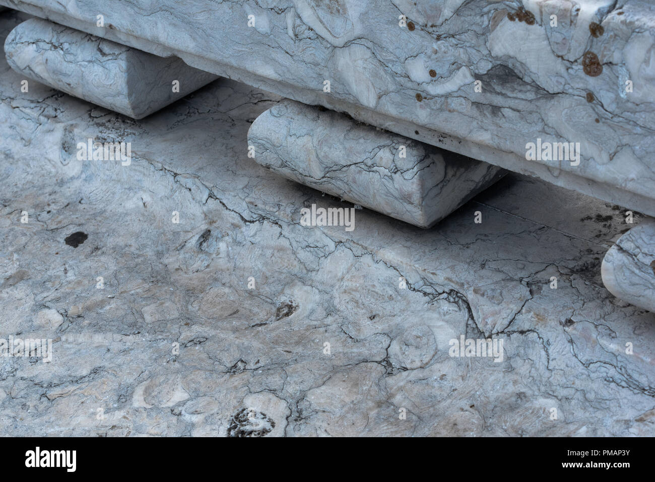 Close-up Detail der öffentlichen Parkbank in weißem Marmor mit ausgeprägten Adern und verwitterten Risse mit zurück mit kleinen Blöcken unterstützt. Stockfoto