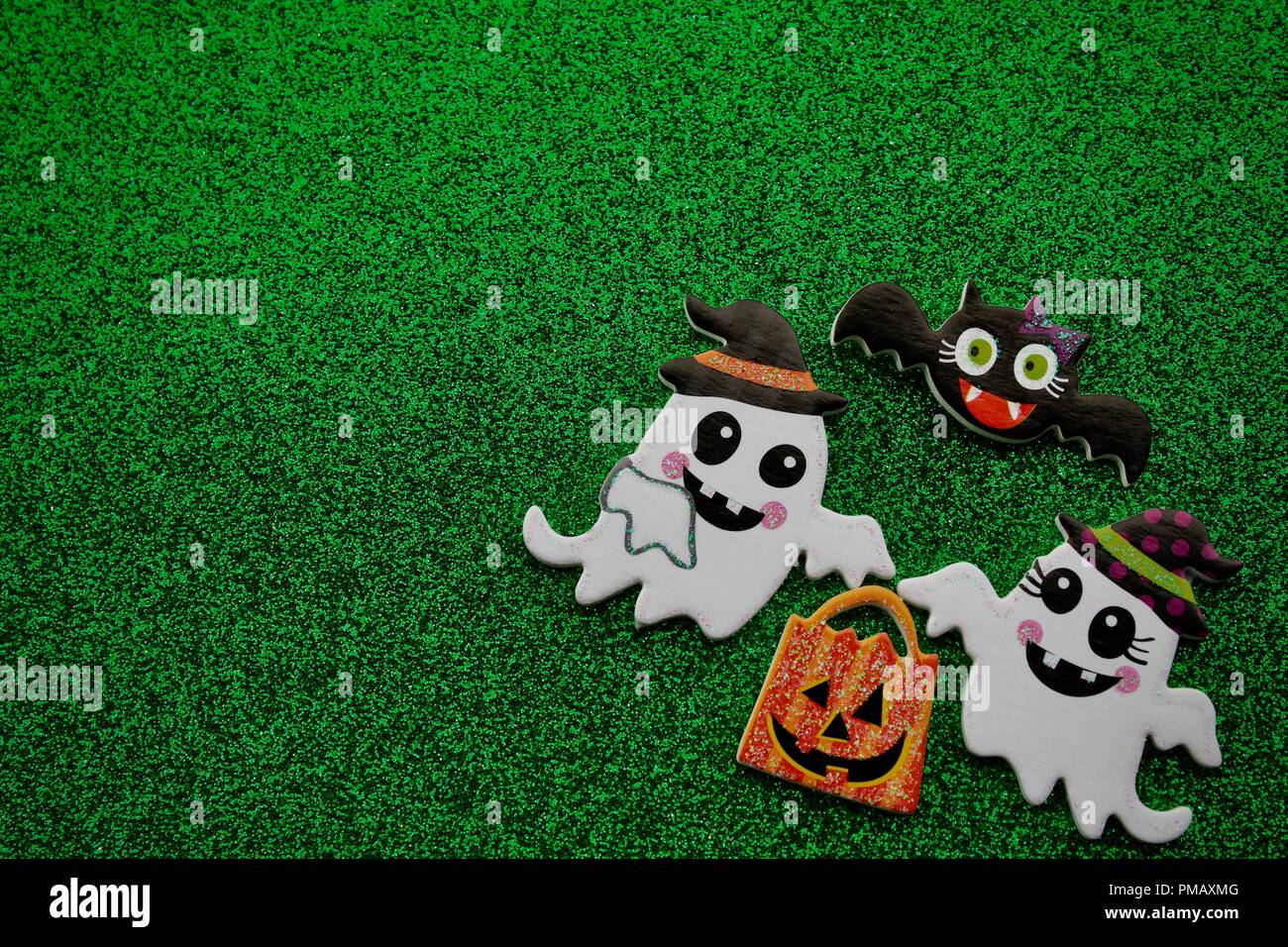 Zwei Geister mit einem Kürbis Trick or treat Tasche mit einer schwarzen Fledermaus oben fliegen mit grünem Hintergrund Stockfoto