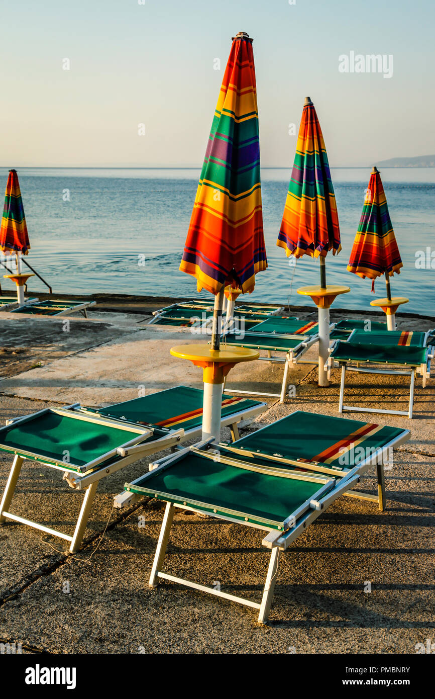 Leere Liegestühle mit großen Heruntergeklappt Sonnenschirme säumen die Uferpromenade am Sonnenuntergang in Opatija an der Adria in Kroatien Stockfoto