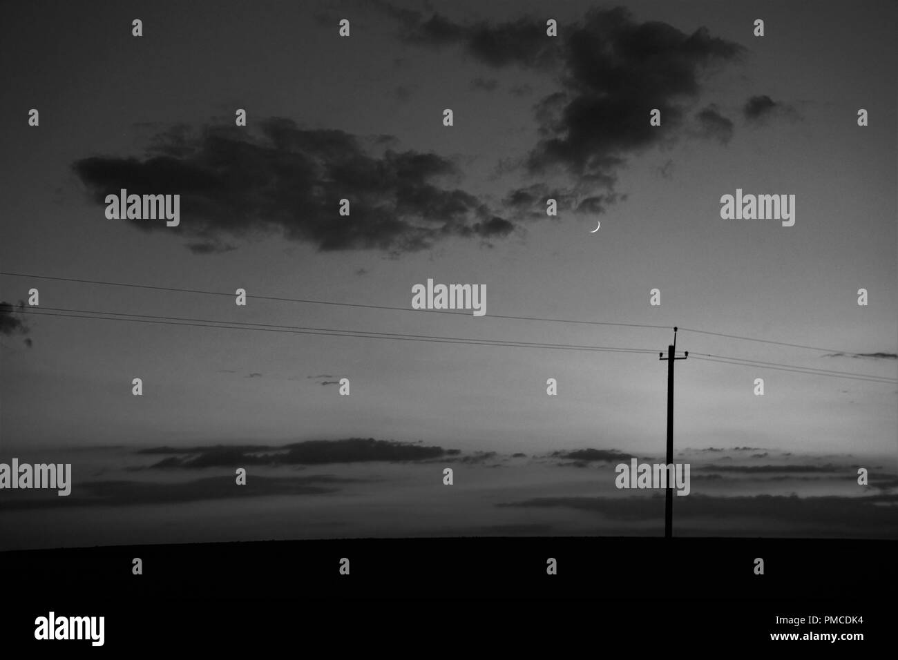 Die Landschaft ist ein neuer Mond und eine elektrische Pole mit Drähten im Feld. Stockfoto