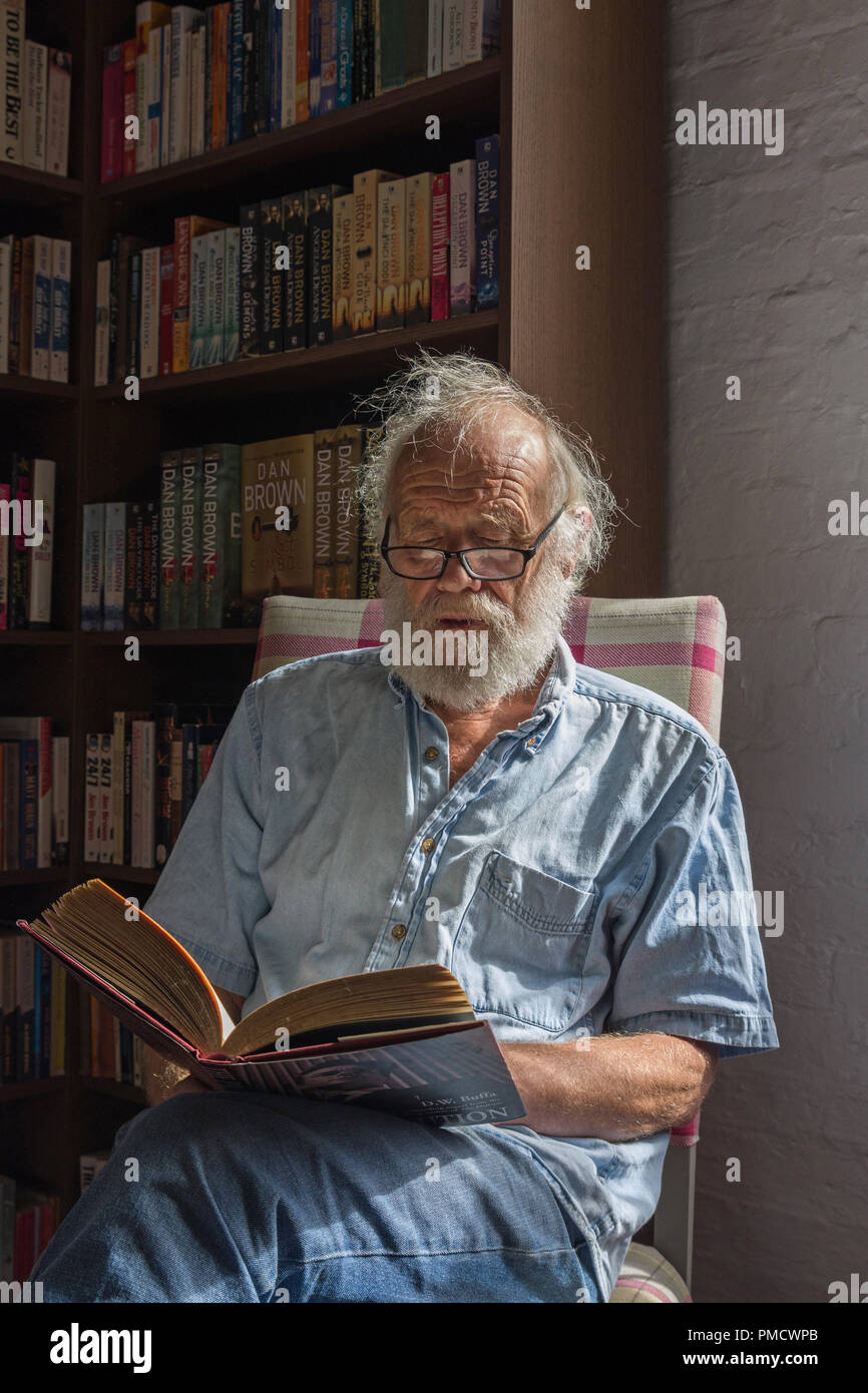 Älterer Mann, sitzen, ein Buch lesen, indem Fenster Licht in einer Buchhandlung. Stockfoto