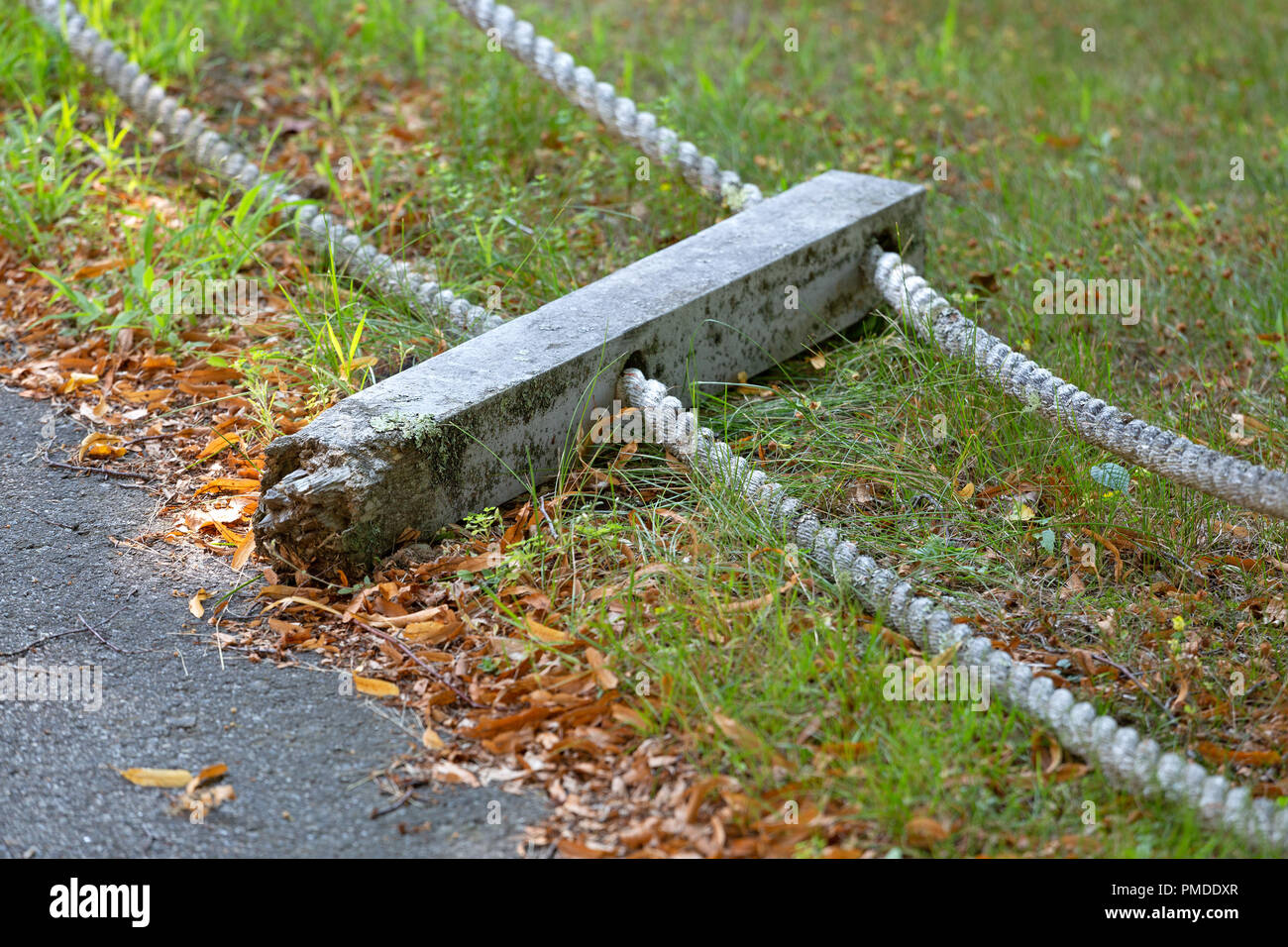 Ein Post gebrochen und an der Basis auf dem Boden und Seil Handläufe neben einer asphaltierten Gehweg verrottete. Stockfoto