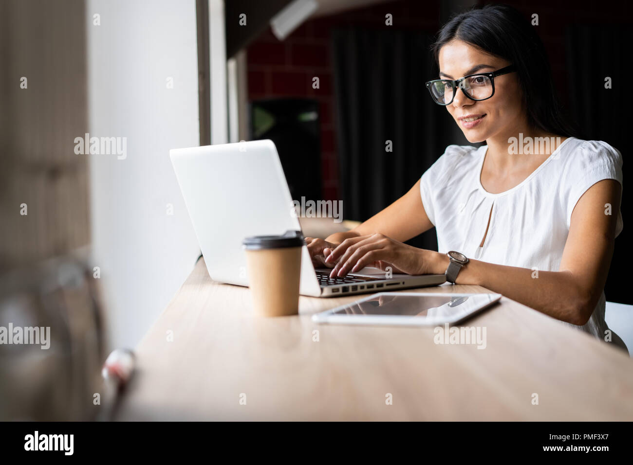 Auf der Suche nach neuen Lösungen. Nachdenkliche junge schöne Geschäftsfrau in Gläsern Arbeiten am Laptop während an Ihrem Arbeitsplatz sitzen Stockfoto