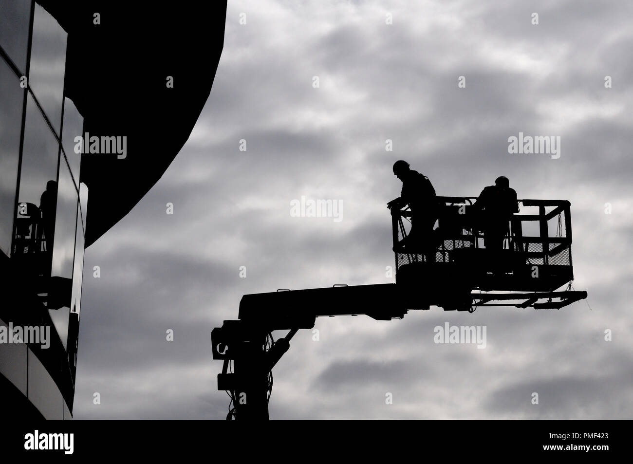 Zwei Bauarbeiter in Silhouette gegen den grauen Himmel über eine hydraulische Hebebühne Stockfoto