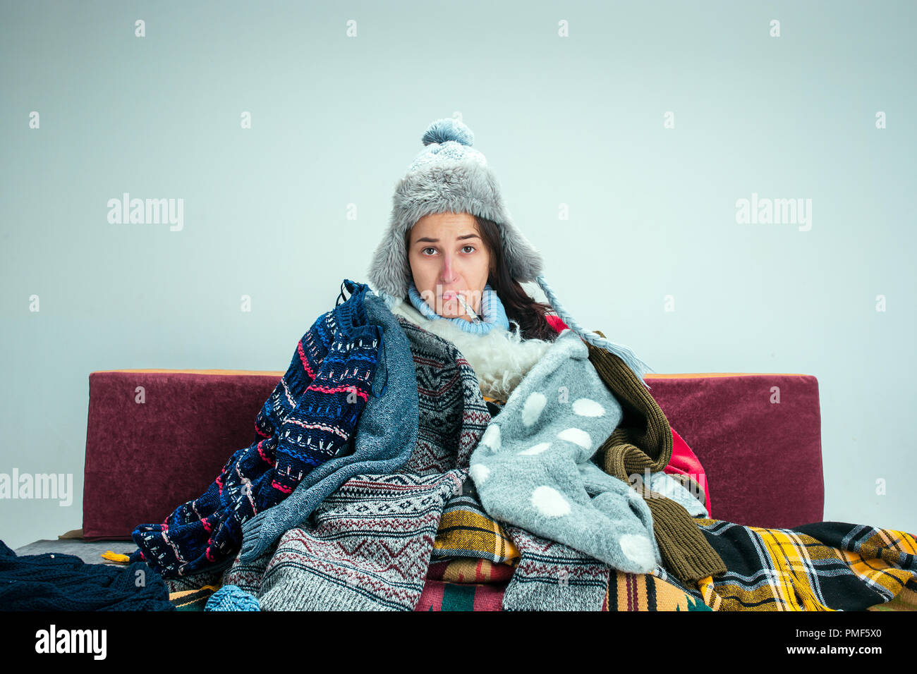 Die junge kranke Frau mit Rauchgas sitzen auf dem Sofa zu Hause oder im Studio mit gestrickten warme Kleidung bedeckt. Krankheit, Grippe, Schmerz Konzept. Entspannung zu Hause. Healthcare Konzepte. Stockfoto