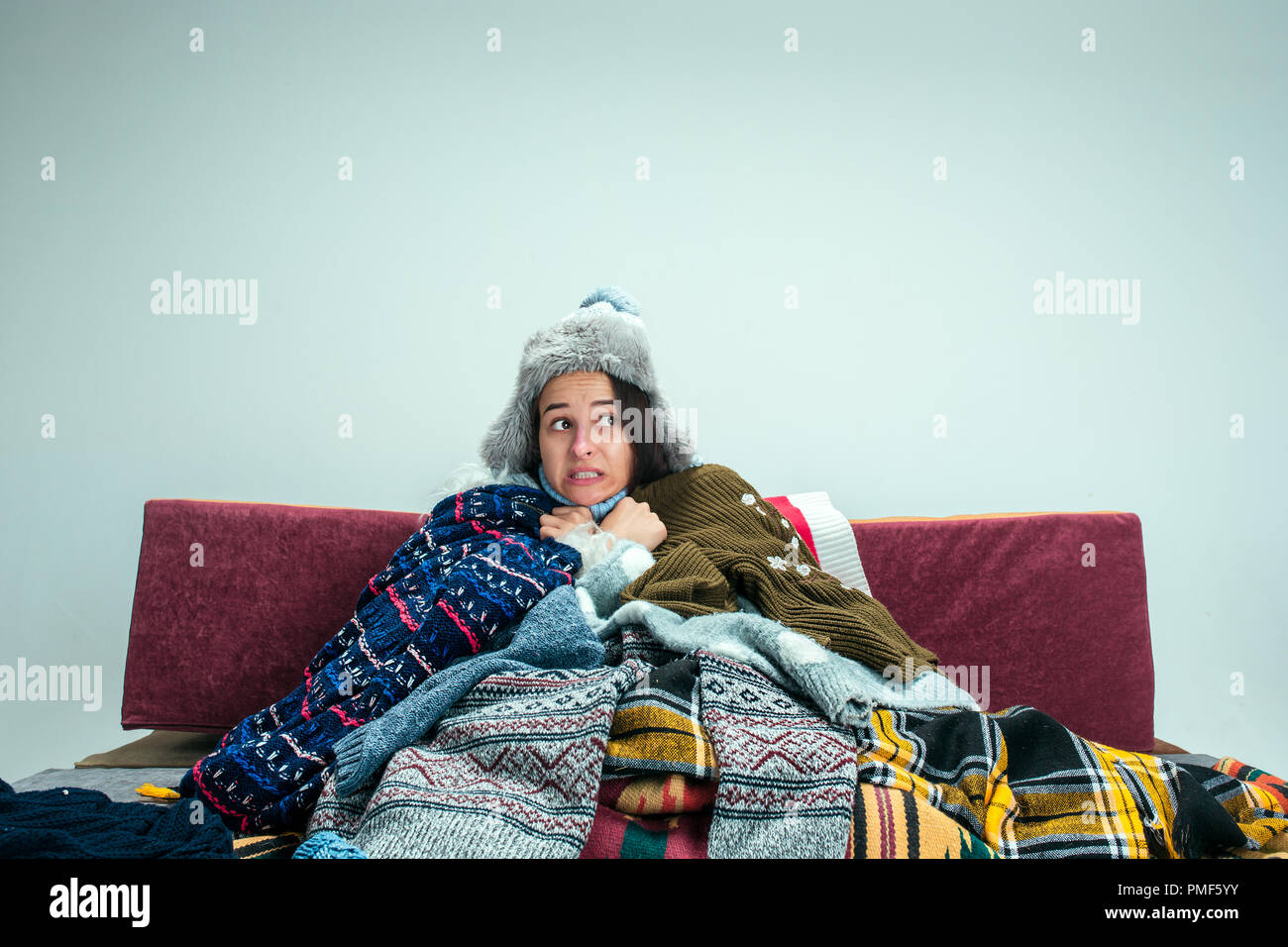 Die junge kranke Frau mit Rauchgas sitzen auf dem Sofa zu Hause oder im Studio mit gestrickten warme Kleidung bedeckt. Krankheit, Grippe, Schmerz Konzept. Entspannung zu Hause. Healthcare Konzepte. Stockfoto
