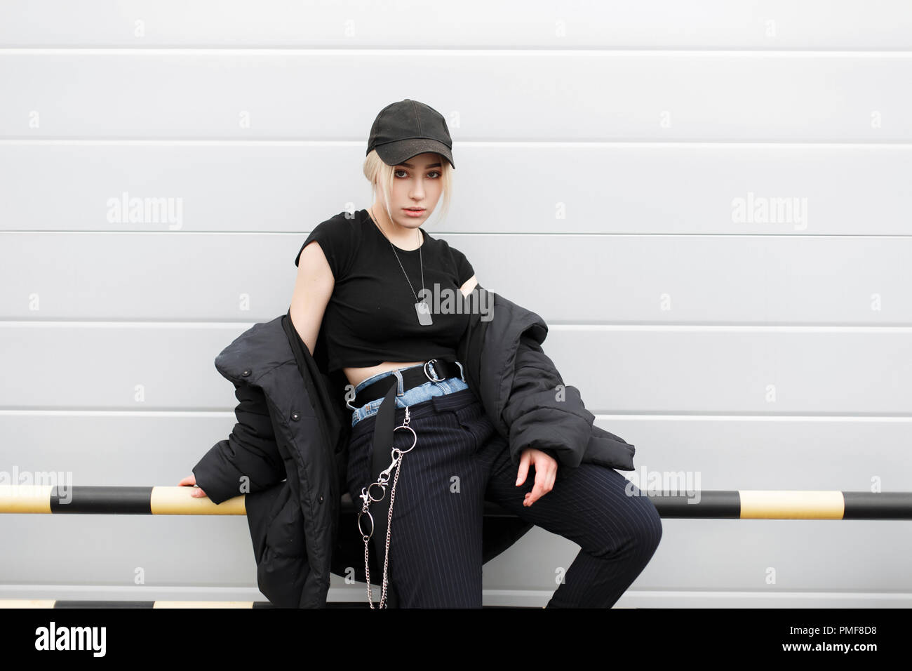 Schöne junge Modell Frau in der Mode elegante schwarze Kleidung, die mit einem Deckel und Winter Jacke auf der Straße sitzt Stockfoto