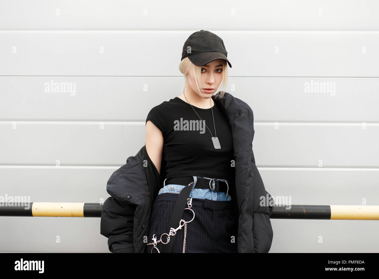 Schöne junge Modell Frau in Schwarz modischer Hut und stilvolle Winter Jacke mit Designer Jeans Hosen auf der Straße in der Nähe der Wand posieren Stockfoto