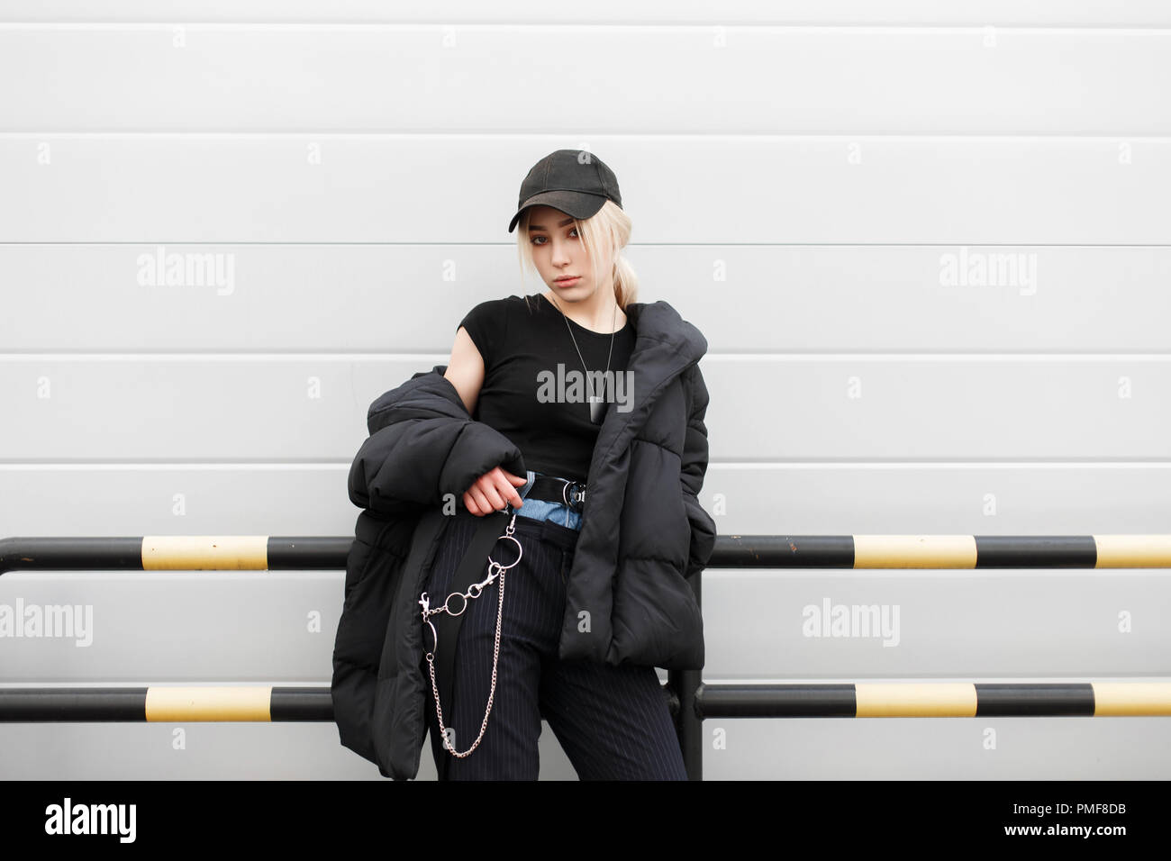Schöne modische Mädchen mit einer schwarzen Kappe und ein stilvolles Winter Jacke mit fashion jeans - Hosen in der Nähe der Wand posieren Stockfoto