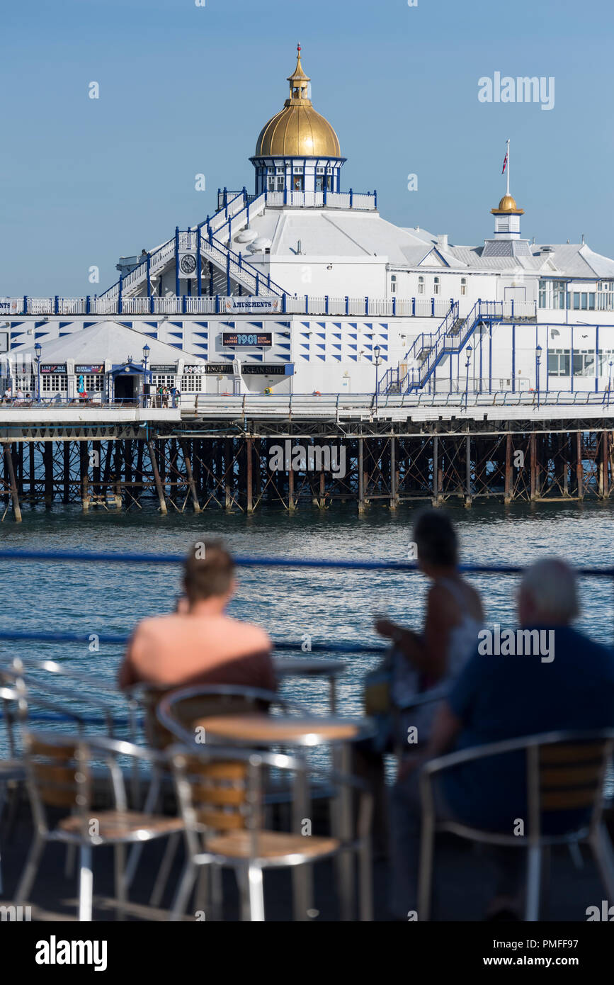 Leute an einem open Air Cafe an der Küste von Eastbourne, in der Grafschaft East Sussex an der Südküste von England mit der Pier im Hintergrund Stockfoto