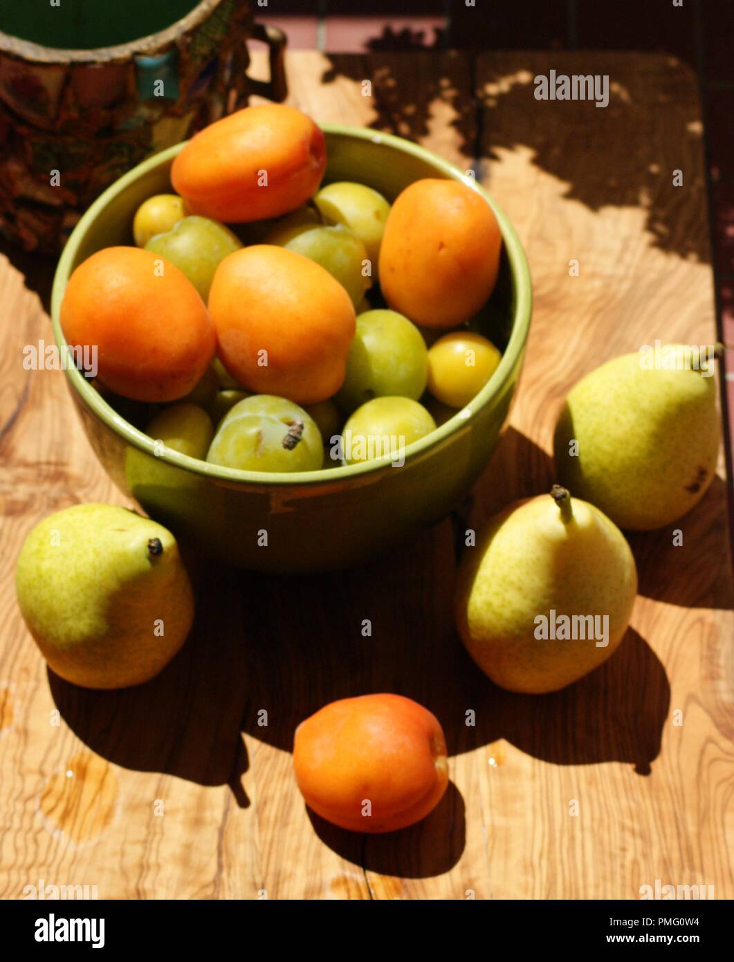 Mise en scène d'une décoration avec des Aprikosen, poires dans un Bol vert avec un Verre de jus d'Orange sur une plance en bois, Inszenierung einer decoratio Stockfoto