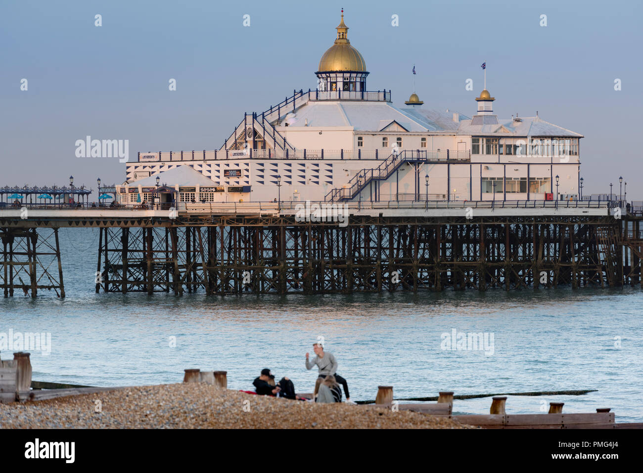 Die Menschen an der Küste von Eastbourne Strand mit Pier hinter Ihnen, in der Grafschaft East Sussex an der Südküste von England in Großbritannien. Stockfoto