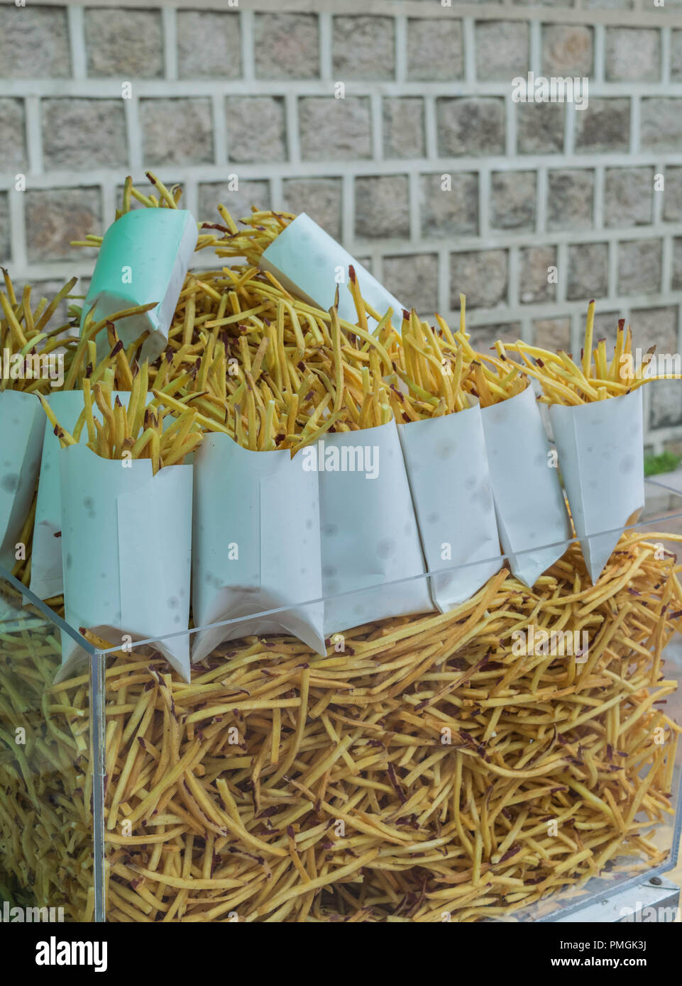 Isolierte Schuß von Pommes frites, einige lose, einige in Boxen, mit einer Mauer im Hintergrund Stockfoto