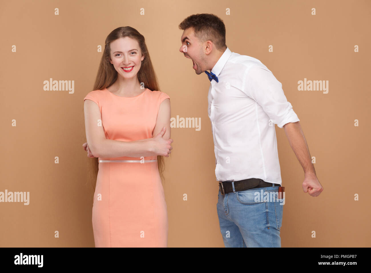 Verrückter junger Mann in weißem T-Shirt stehen und schreit Frau im rosa Kleid. Frau, die sich nicht interessieren, und wenn man die Kamera mit toothy Lächeln. indoor Studio s Stockfoto