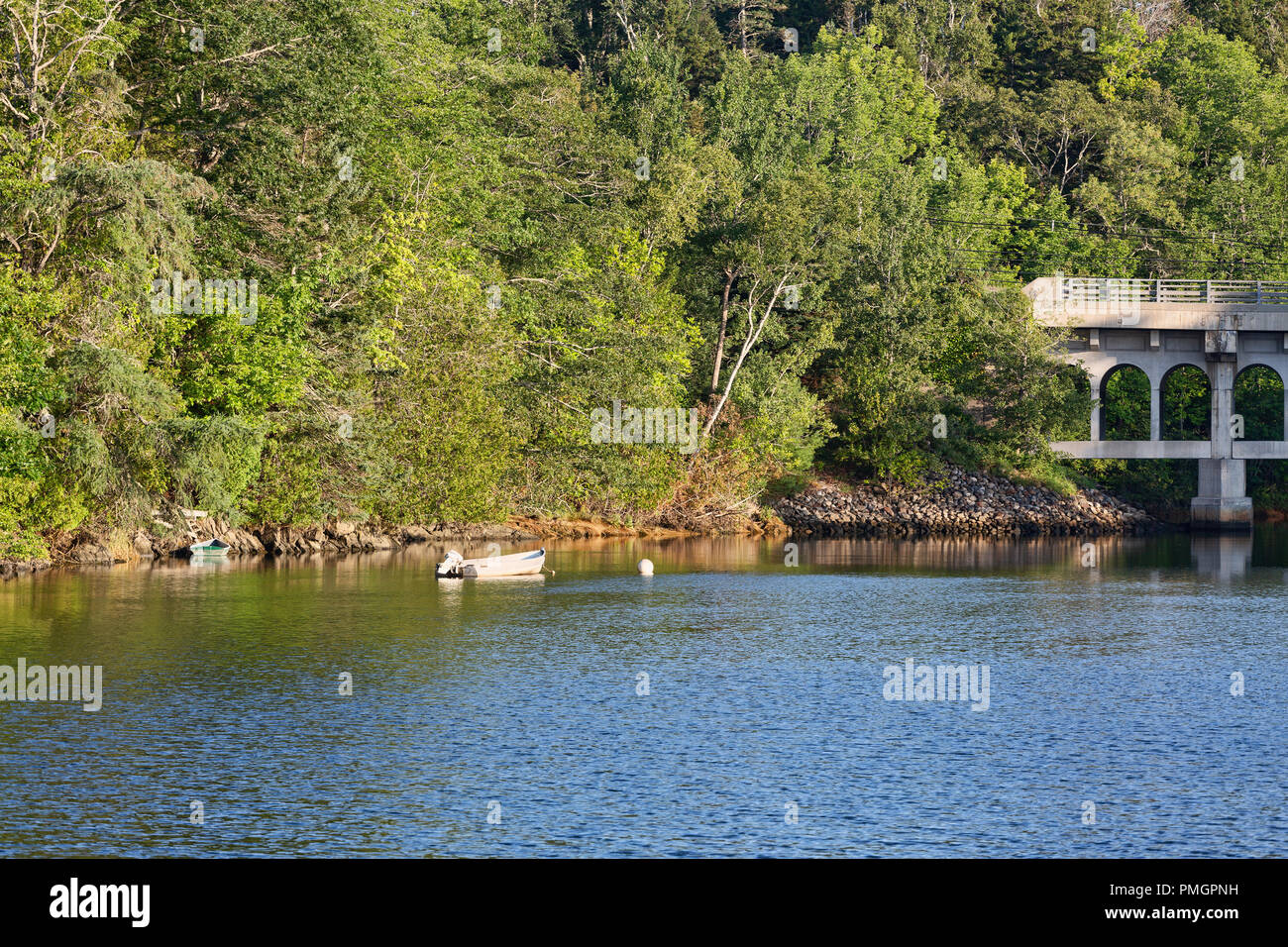 Einem verankerten Skiff und ein weiteres an die Bank von einem Tidal River mit einer Brücke im Hintergrund gebunden an der Küste von Maine im Sommer. Stockfoto