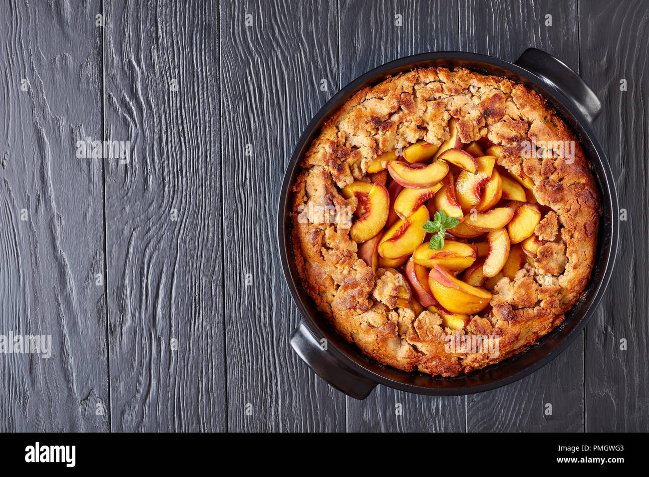 Einfache und gesunde peach Cobbler gebacken in einem schwarzen Auflaufform, auf einem schwarzen Holz- Tabelle, Ansicht von oben, flach Stockfoto