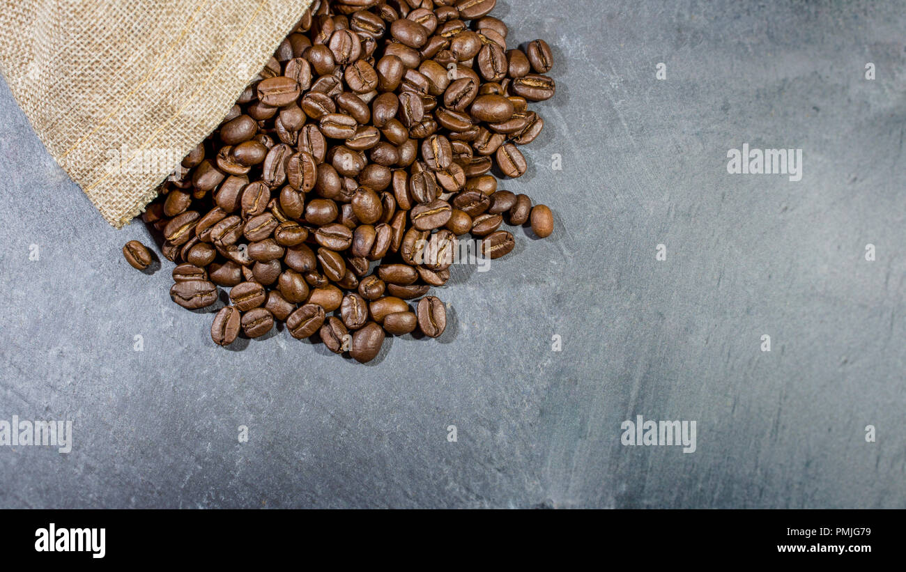 Sackleinen sack überfüllt mit gerösteten Kaffeebohnen und in grauem Schiefer Stein Oberfläche Hintergrund. Mit kopieren. Stockfoto
