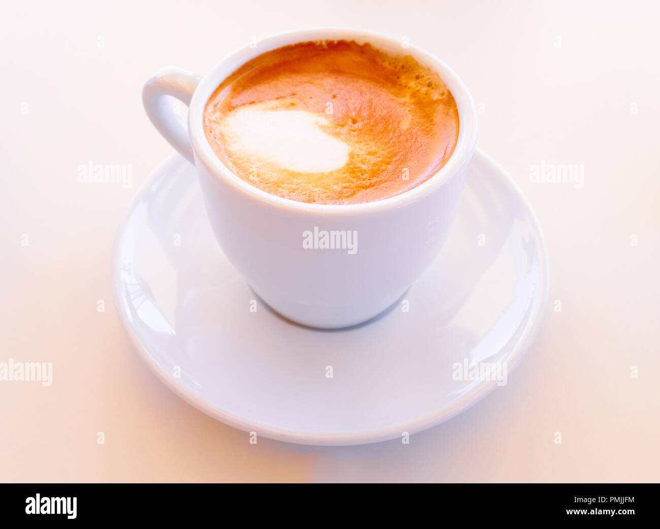 Kleine trinken trinken starken Kaffee mit Milch in eine weiße Keramik Tasse mit Untertasse Stockfoto