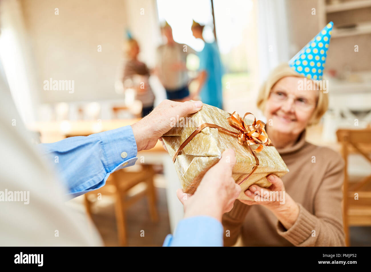 Ältere Frau mit einem Geschenk an Ihrer Geburtstagsfeier im Seniorenheim überrascht Stockfoto