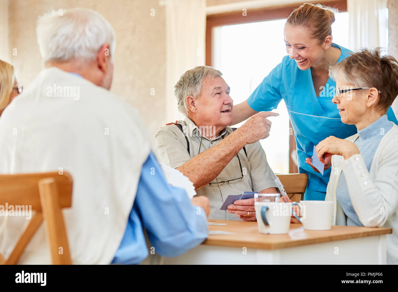 Krankenpflege Dame hat Spaß mit einer Gruppe von Senioren Spielkarten im Pflegeheim Stockfoto