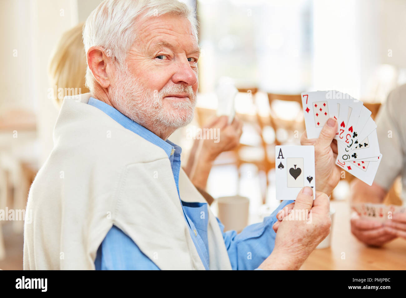 Älterer Mann zeigt ein Ace wenn die Karten mit Freunden im Ruhestand home Stockfoto