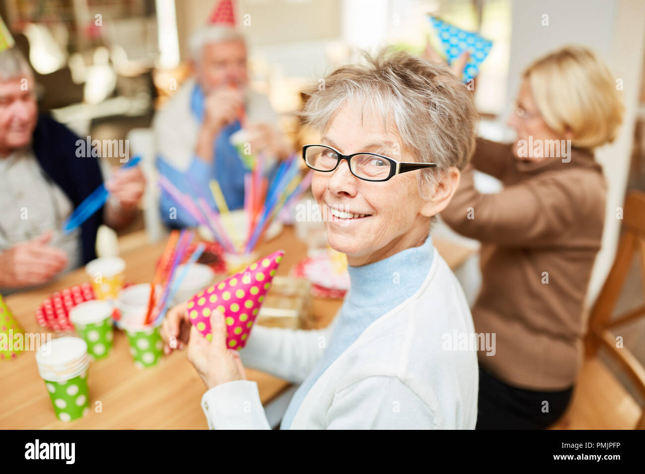 Ältere Frau im Seniorenheim feiert Karneval oder Geburtstag zusammen mit Freunden Stockfoto