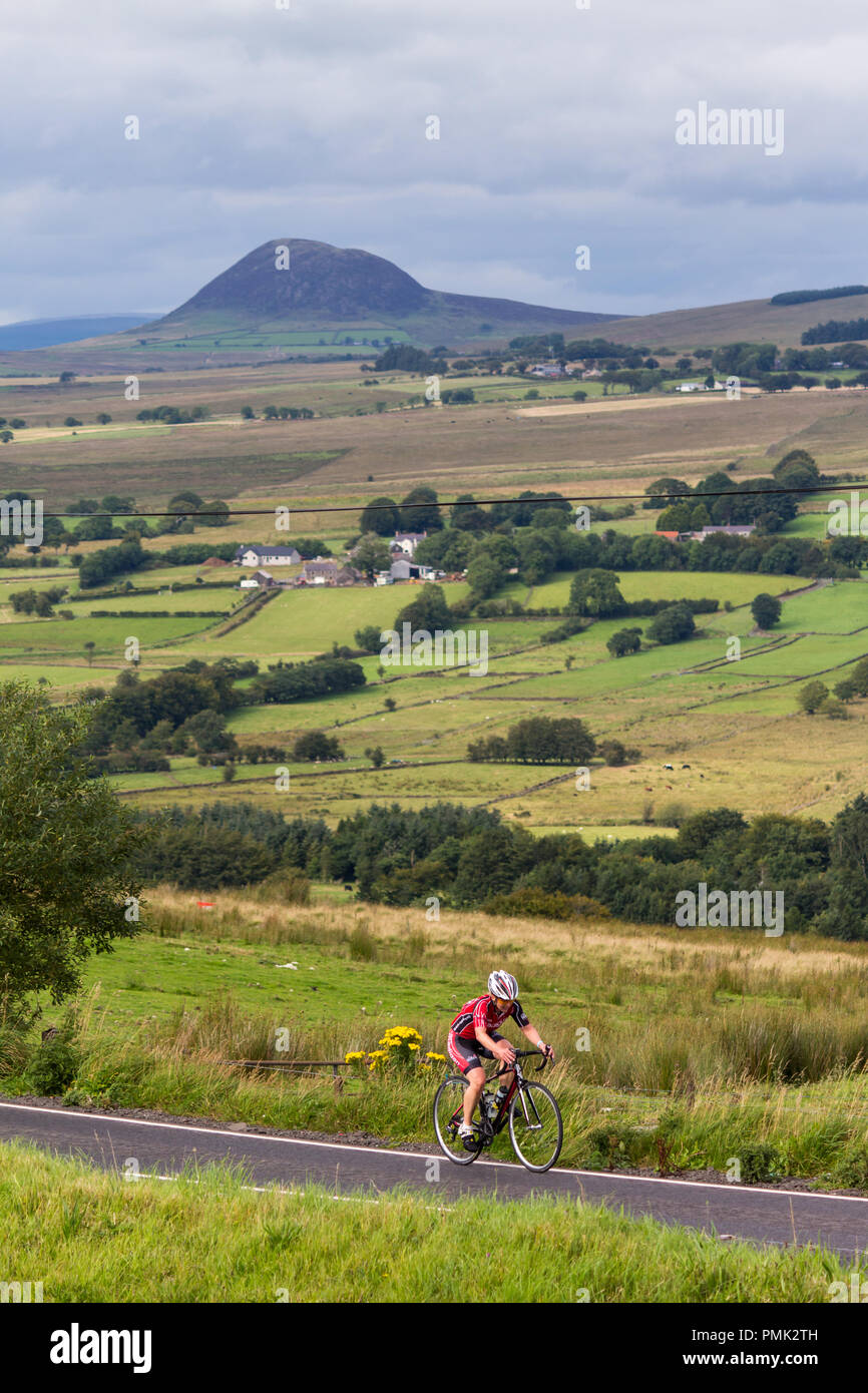 Ein Radfahrer aufsteigend Große Collin Hügel mit Blick zum Slemish Mountain in der Entfernung, in der Nähe von Ballymena, County Antrim, Nordirland. Stockfoto