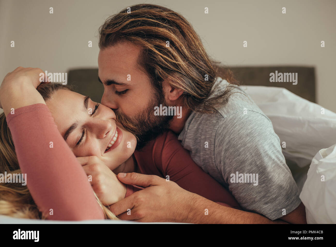 Mann küsste seine Frau schlafend auf dem Bett. Paar im Bett in Decke mit Mann und seinem Partner abgedeckt. Stockfoto