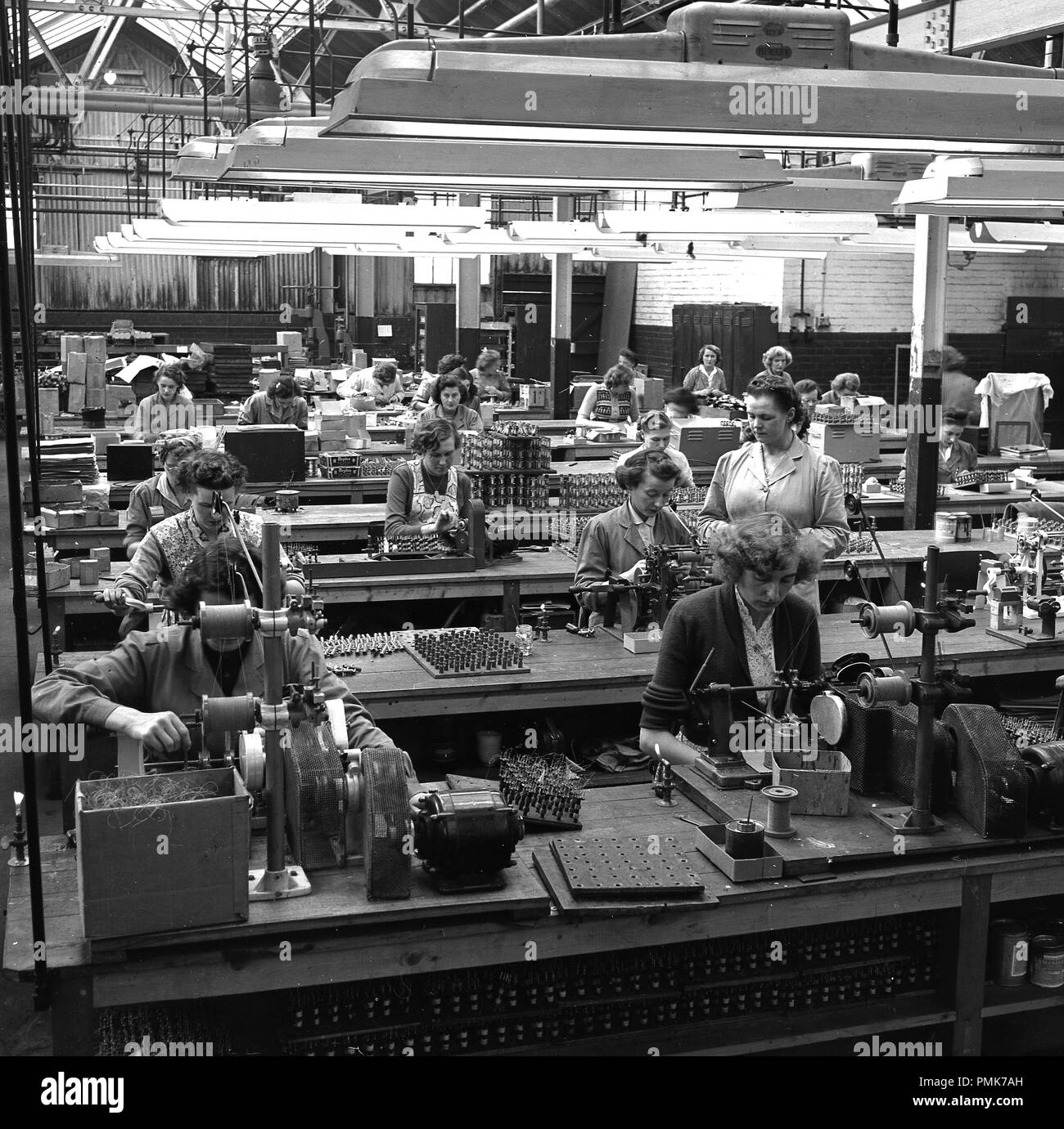 1959 s, historischen, weibliche Arbeitnehmer auf Bänken sitzen, einige mit Industrial sewing mchines, auf dem Shop floor an der stets bereit ist, batterie Fabrik in Walthamstow, London, England, UK. Im Bild zu sehen ist eine weibliche Vorgesetzte Überprüfung der Arbeit einer Frau in einem Tuch auftragen. Stockfoto