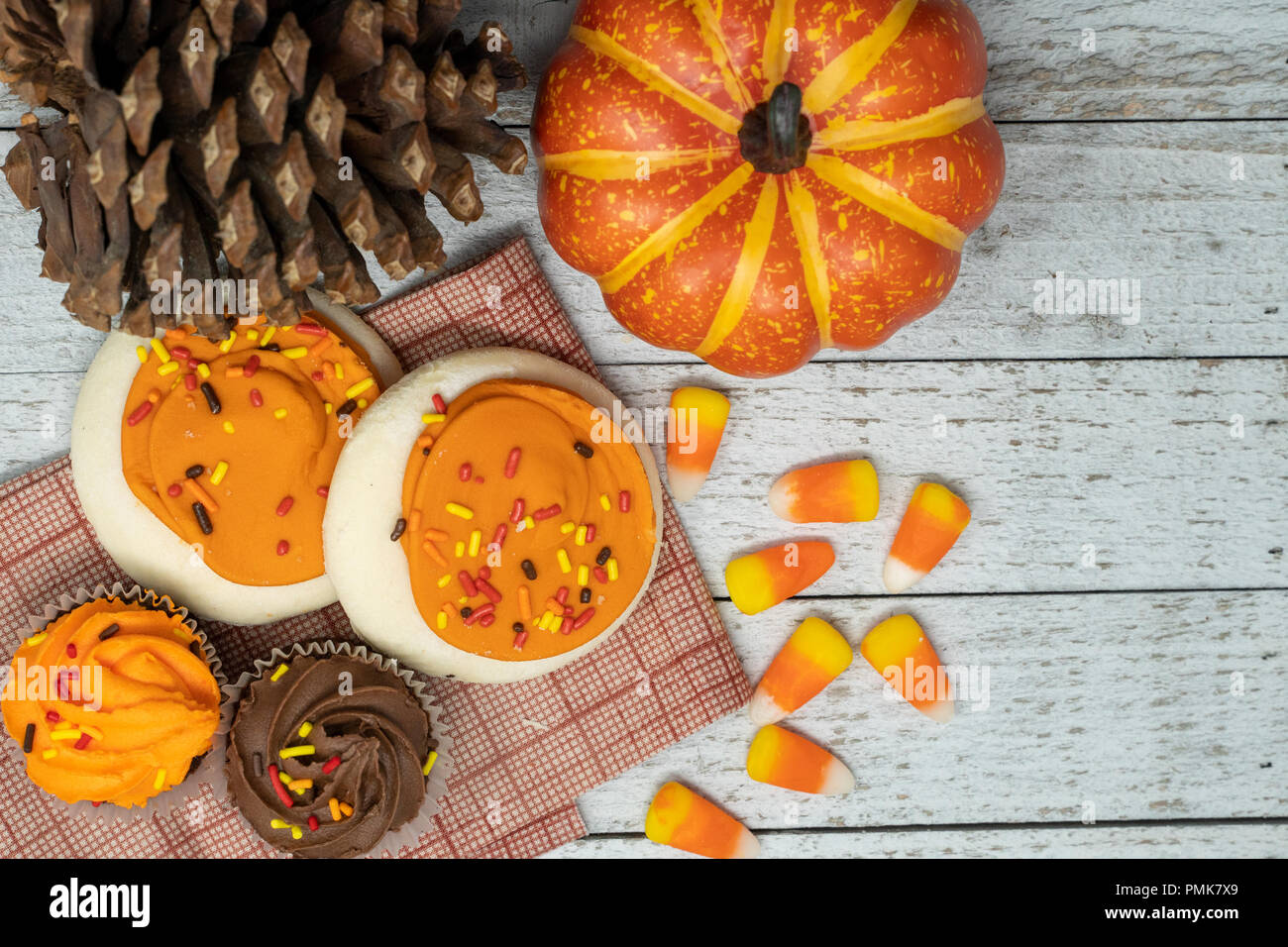 Orange iced Sugar Cookies und Halloween themed Cupcakes - Verstreut candy Corn. Tannenzapfen und Kürbisse, Holz- Hintergrund. Konzept für den Herbst Stockfoto