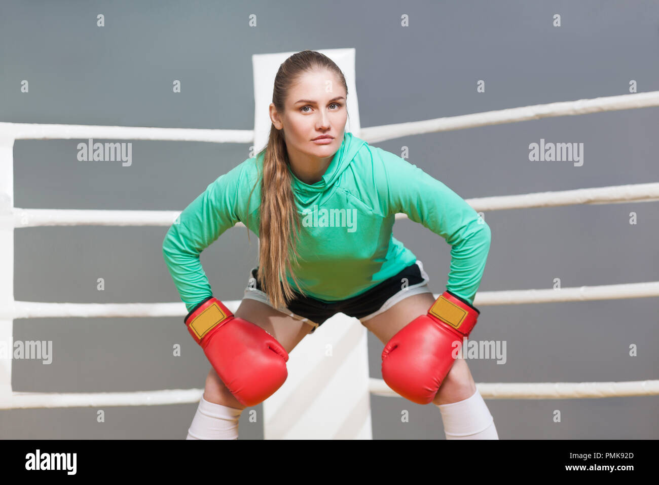 Wütend Boxing athletische junge Frau in grün Langarm poising mit roten Boxhandschuhe und Kamera mit ernsten Gesicht. indoor studio Schuß auf g Stockfoto