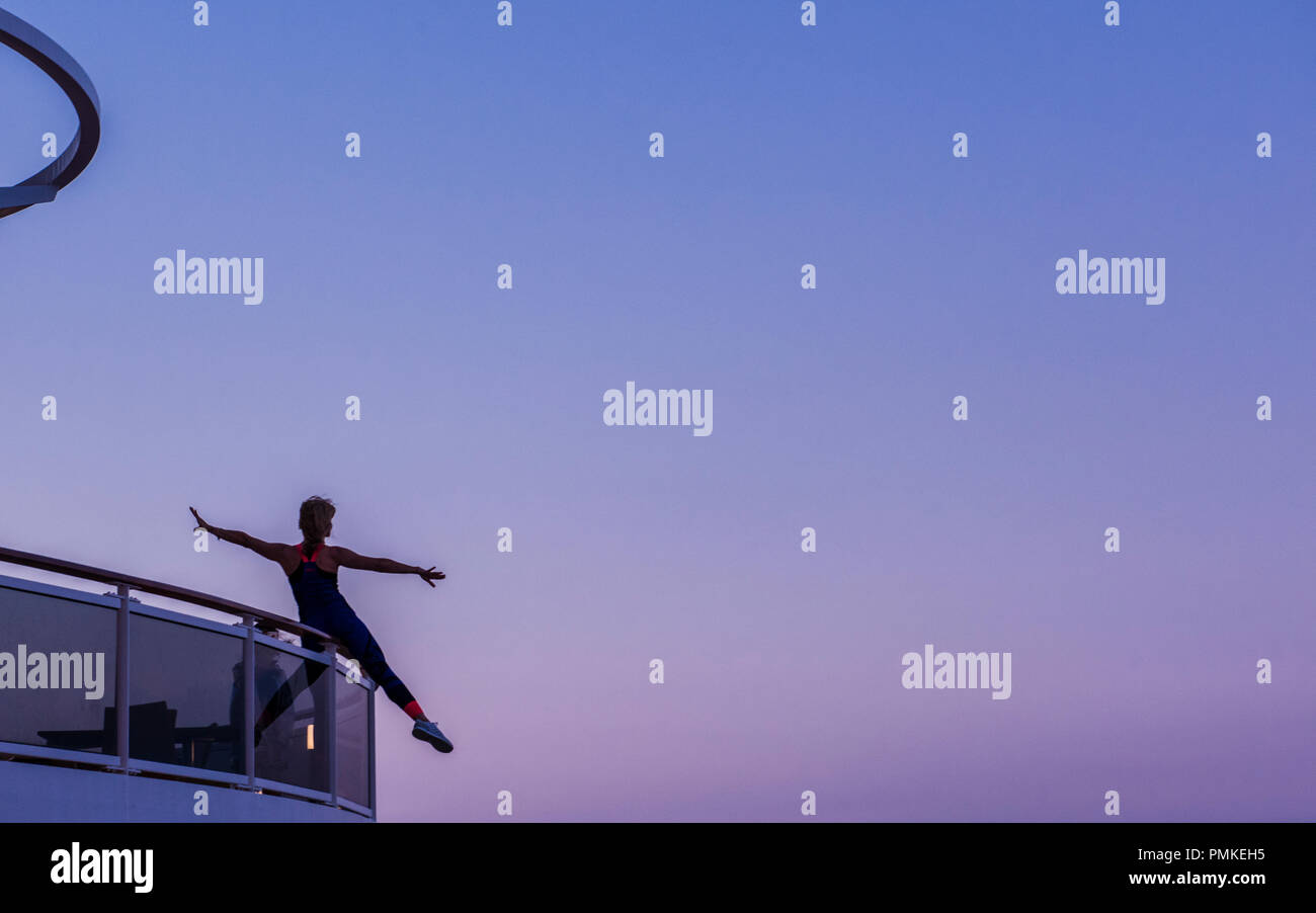 Frau balancing und Stretching auf der Brücke von Kreuzfahrtschiff MSC Seaview, bei Sonnenuntergang Stockfoto