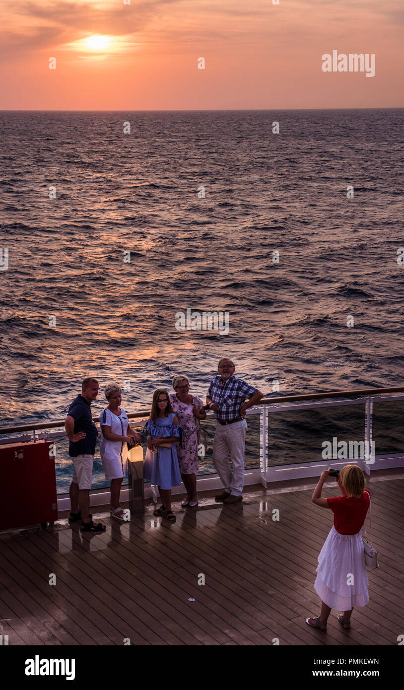 Frau unter Gruppenfoto mit dramatischen orange Sonnenuntergang im Hintergrund, an Deck der Kreuzfahrtschiff MSC Seaview Stockfoto