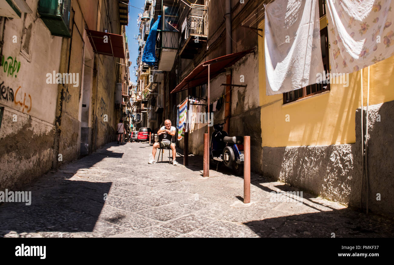 Mann sitzt vor dem Haus in einer alten Gasse in der Mitte der Stadt, Neapel, Italien, Europa Stockfoto