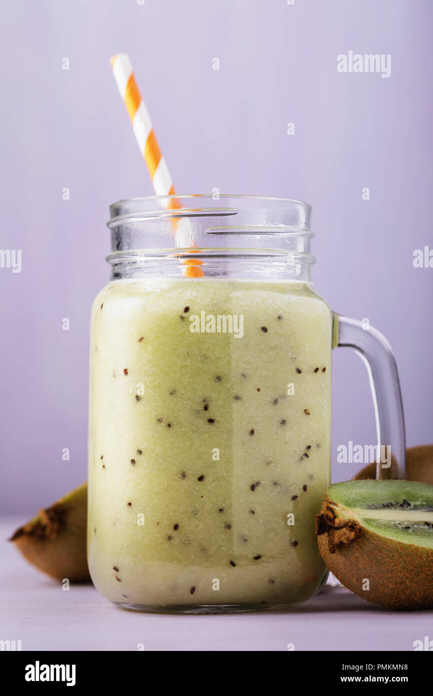 Smoothies aus reifen Kiwi in einem durchsichtigen Glas mit Obst auf Violett Hintergrund zubereitet Stockfoto