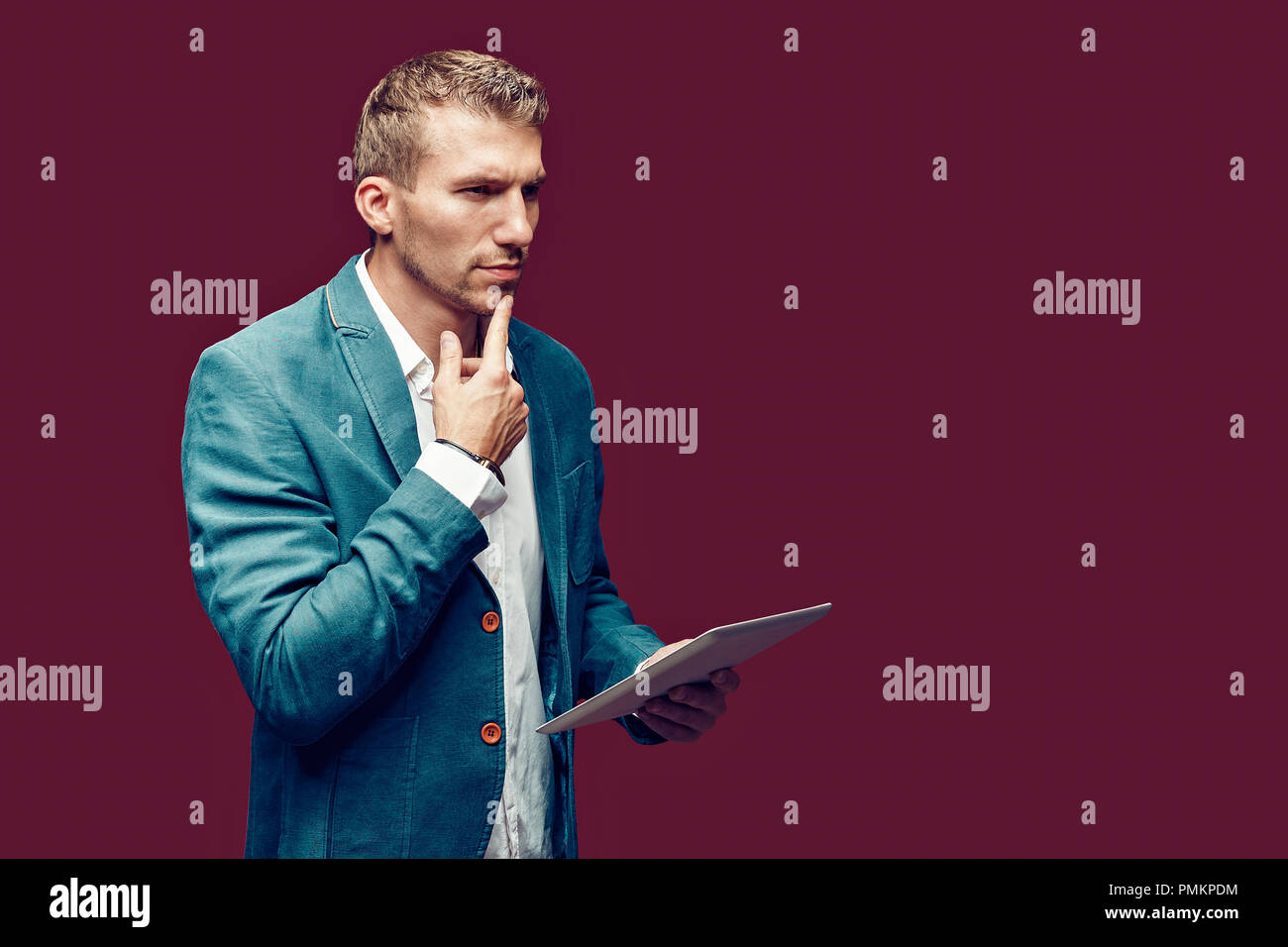 Junge Bartgeier nach Business Mann hält Tablet Computer denken und berühren Bart weg an Copyspace über den roten Hintergrund konzentriert. Stockfoto