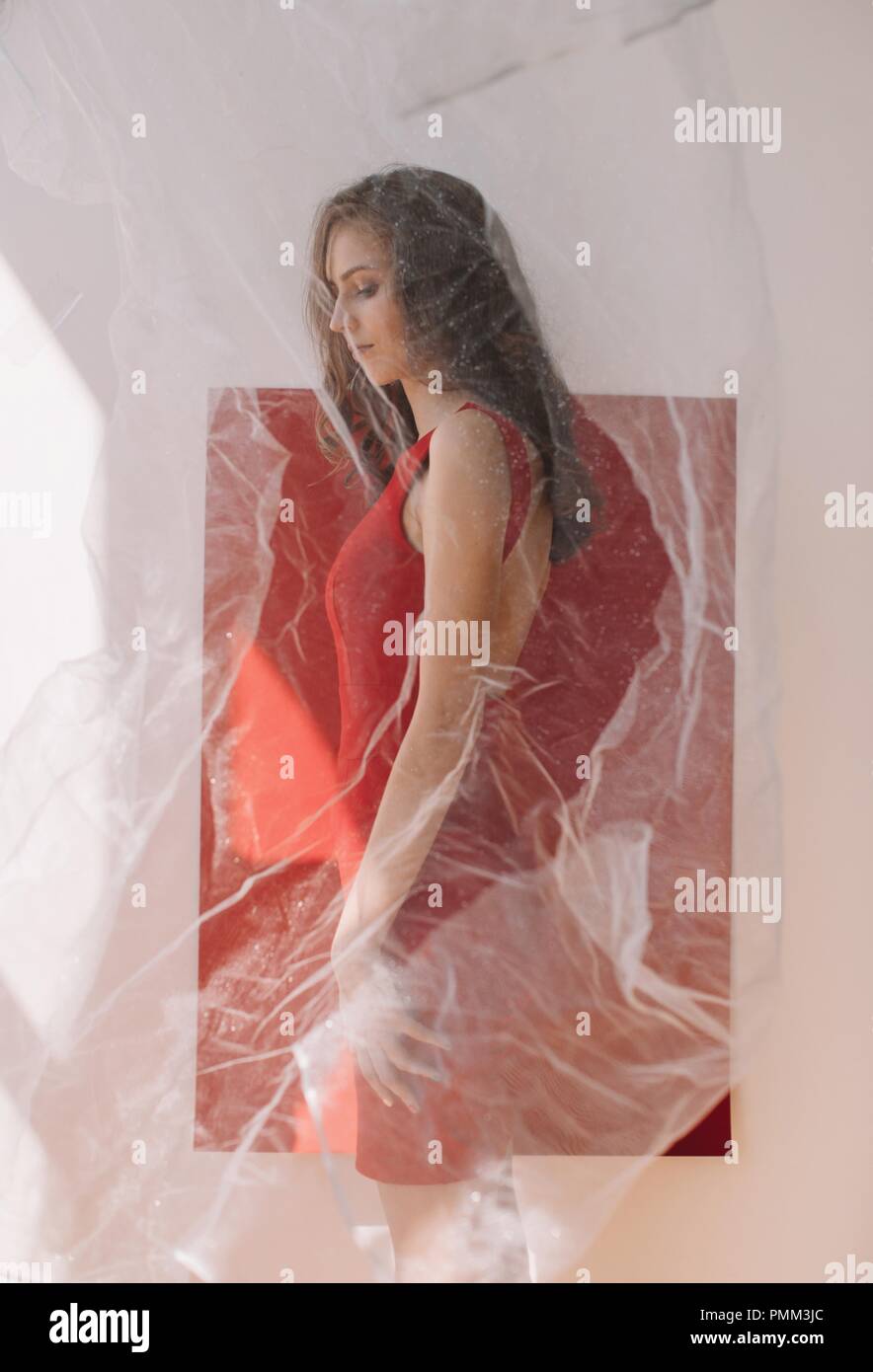Porträt einer Frau, die durch eine rote Wand hinter einem Schleier stehend Stockfoto