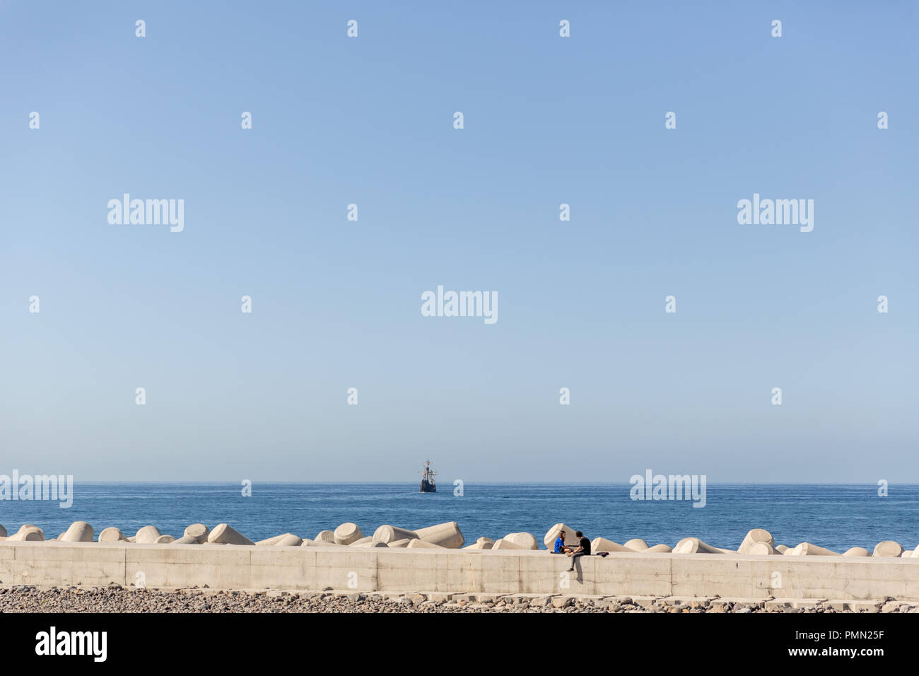 Heterosexuelles Paar heraus zusammen hängen, auf dem Meer, mit sehr blauen Meer und ein Segelschiff in der Ferne Stockfoto