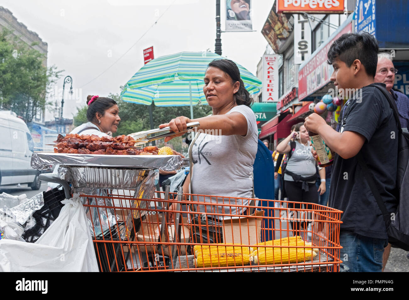 Eine Frau auf einer belebten Straße in Jackson Heights, Queens verkauf Spieße mit Fleisch und Mais. In Stockfoto