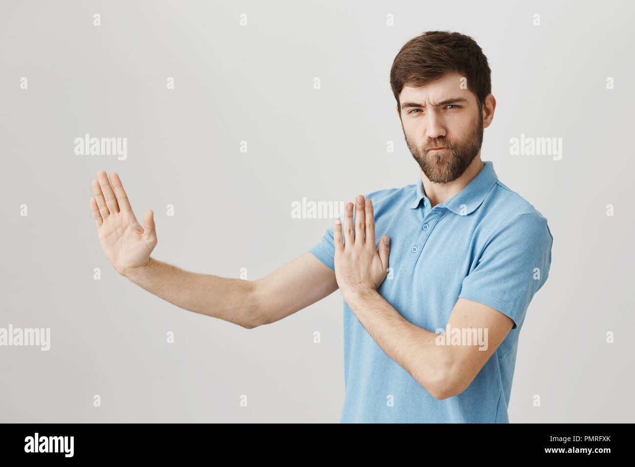 Portrait von verspielten charmante europäische Mann, wie Ninja oder Karate Kämpfer handelt, stehen die Hälfte - in der Verteidigung gedreht Pose mit angehobenen Palmen und zuversichtlich an der Kamera, wie professionelle Stockfoto