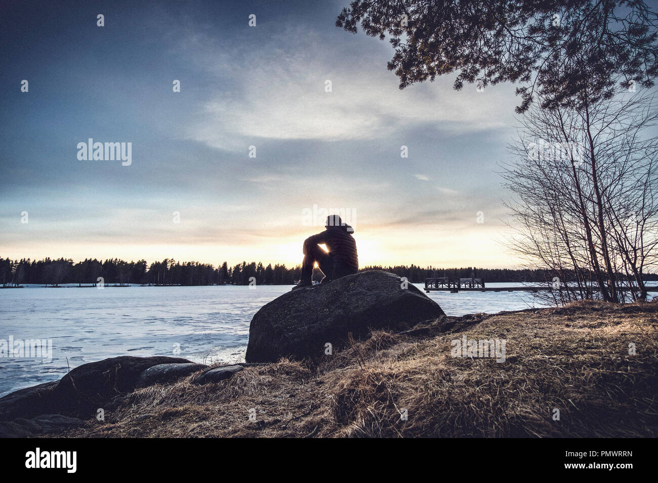 Mann auf Felsen mit Blick auf den See Nydala, Umea, Schweden sitzen Stockfoto