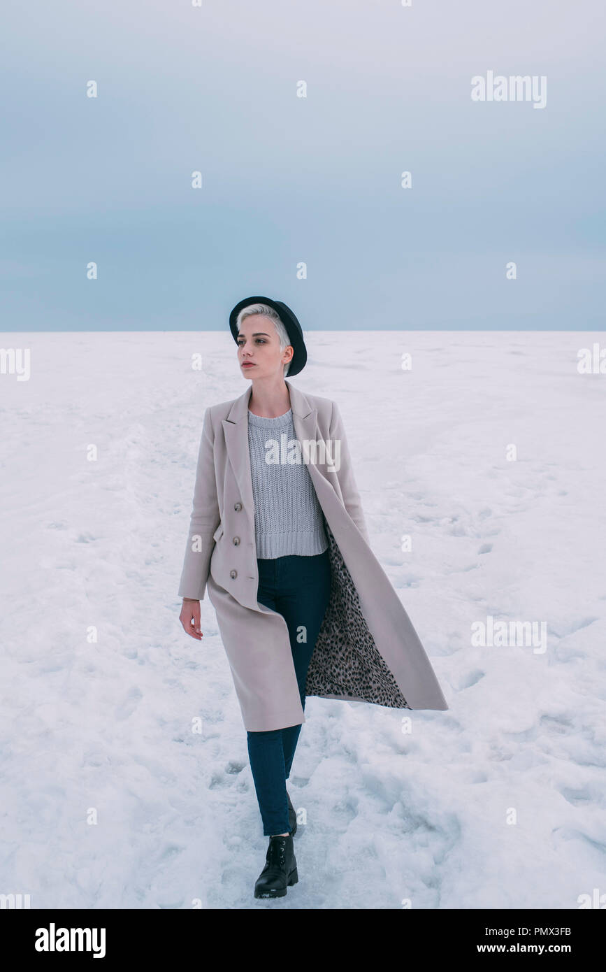 Frau in Mantel und Hut Wandern im Schnee bedeckt die Landschaft Stockfoto